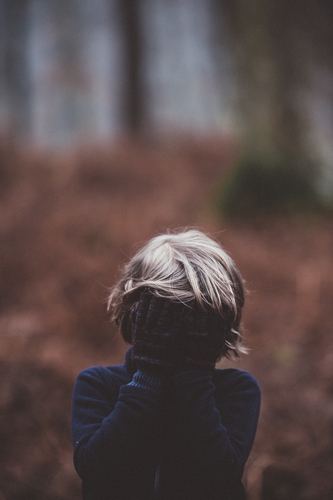 sad child in woods with head in hands