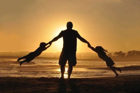 sillhoette of fatheron the beach at sunset swinging his children by the arms