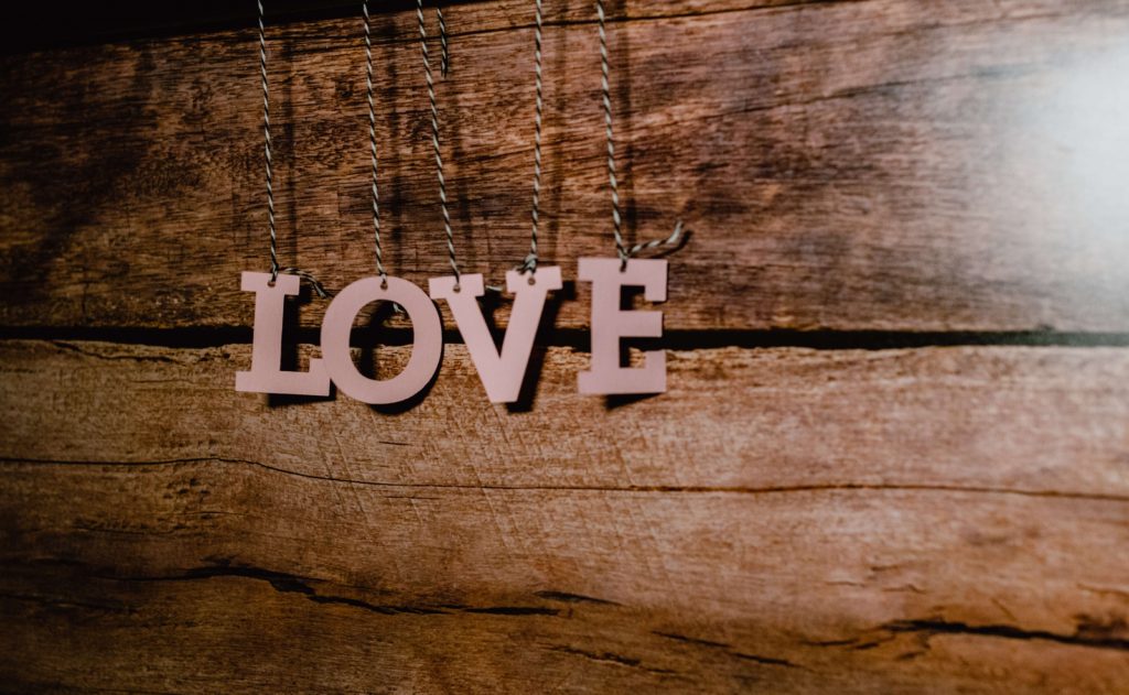 Pink letters spelling LOVE suspended by string against timber backdrop